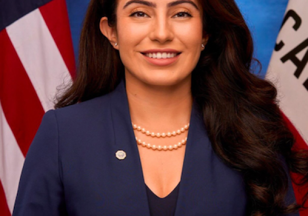 Senator Sasha Renée Pérez wearing a blue blazer standing in front of a United States and California Flag