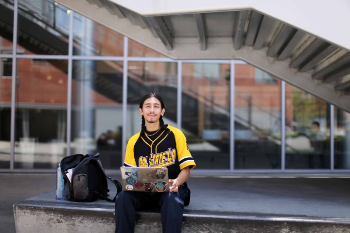 Student in Cal State LA clothing sits confidently outside while using computer