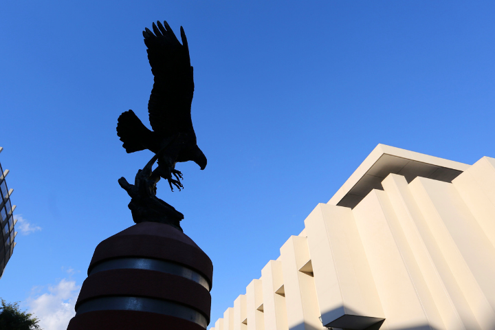 Eagle statue and white building behind. Backdrop is a blue sky